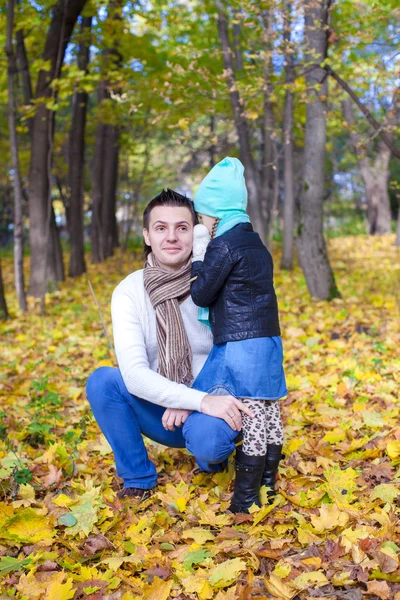 Young father and his cute little daughter whispering in autumn park — Stock Photo, Image