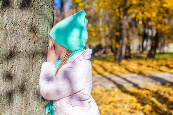 Niña jugando al escondite cerca del árbol en el parque de otoño —  Fotos de Stock