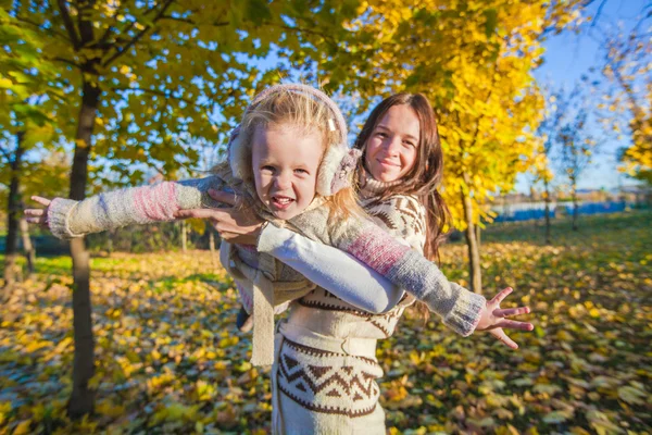 Little adorable girl and young mother having fun in autumn park on sunny day — Stock Photo, Image
