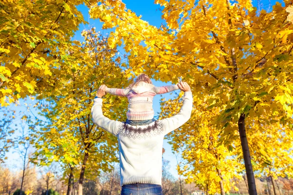 Kleines Mädchen reitet im Herbstpark auf den Schultern des Vaters — Stockfoto