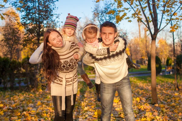 Família de quatro com duas crianças se divertindo no parque de outono em um dia quente ensolarado — Fotografia de Stock