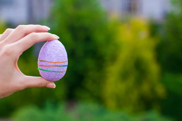 Brillante huevo de Pascua púrpura en la mano sobre el fondo del cielo azul — Foto de Stock
