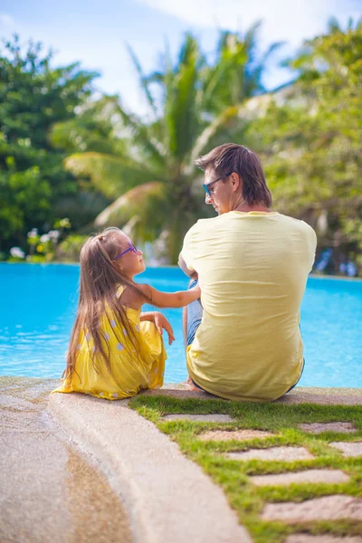 Back view of young father and his cute daughter sitting by the swimming pool — Stock Photo, Image