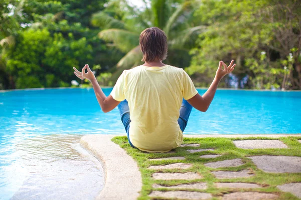 Young man sitting in lotus position near the swimming pool — Stock Photo, Image