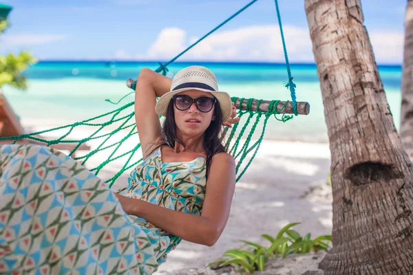 Junge Frau sitzt an der Hängematte im Schatten eines Baumes am Strand — Stockfoto