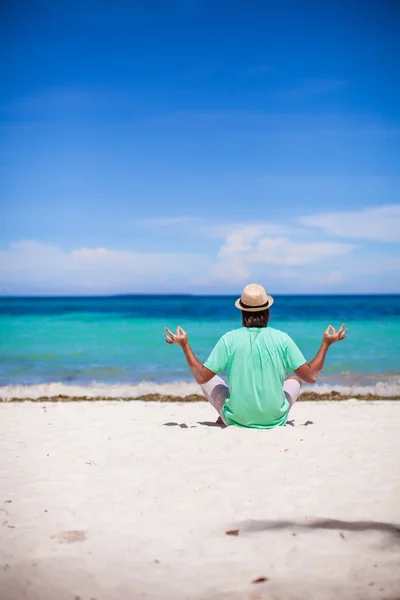 Young man sitting in lotus position on white tropical beach — Stock Photo, Image