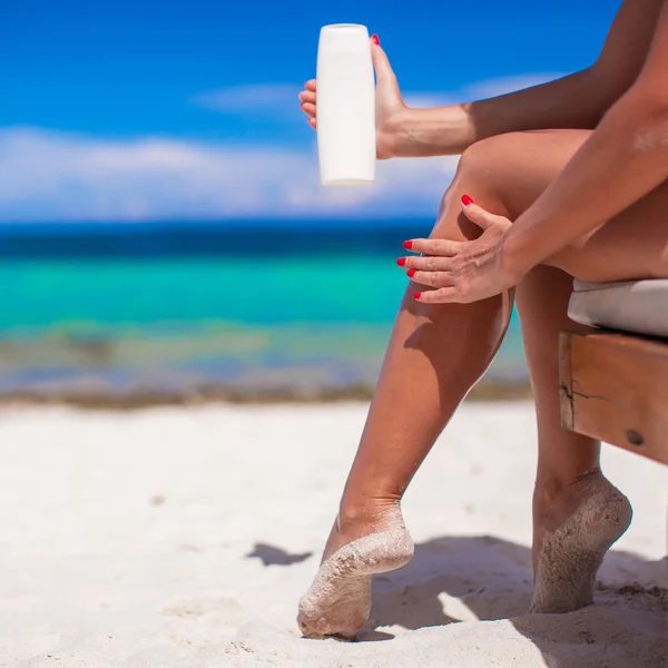 Mujer joven aplicar crema en sus suaves piernas bronceadas en la playa tropical —  Fotos de Stock