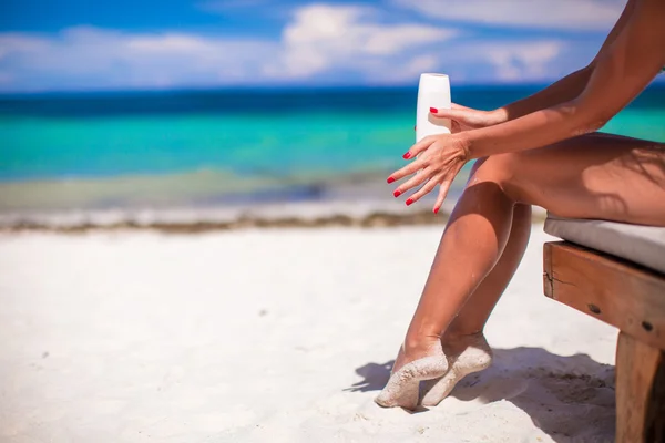 Молода жінка наносить крем на свої гладкі танізовані ноги на тропічний маяк — стокове фото