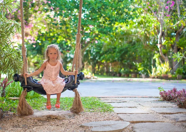 Bambina che oscilla su un'altalena in un accogliente cortile fiorito — Foto Stock