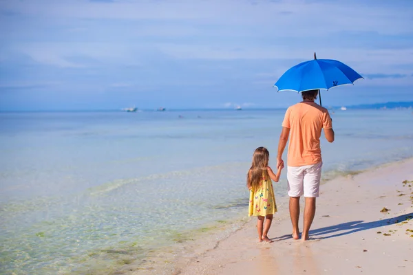 Young father and his adorable little daughter hiding from the sun under a blue umbrella on white sunny day — Stock Photo, Image