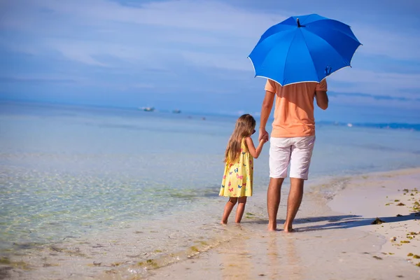 Jovem pai e sua filha caminhando sob um guarda-chuva azul na praia de areia branca — Fotografia de Stock