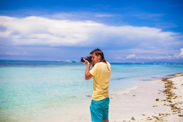 Jeune homme photographiant avec un appareil photo dans ses mains sur une plage tropicale — Photo