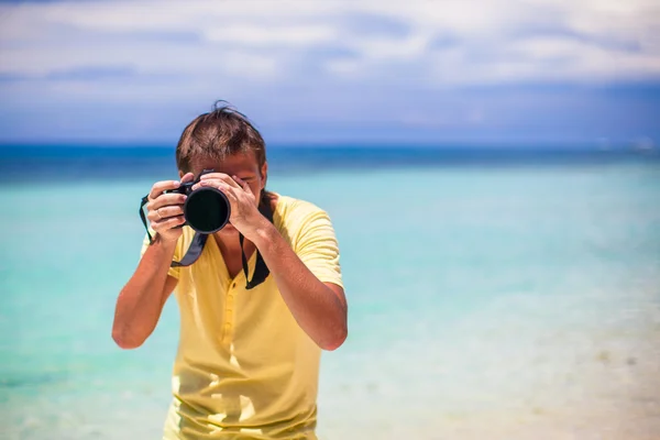 Jovem fotografando com câmera em suas mãos em uma praia tropical — Fotografia de Stock