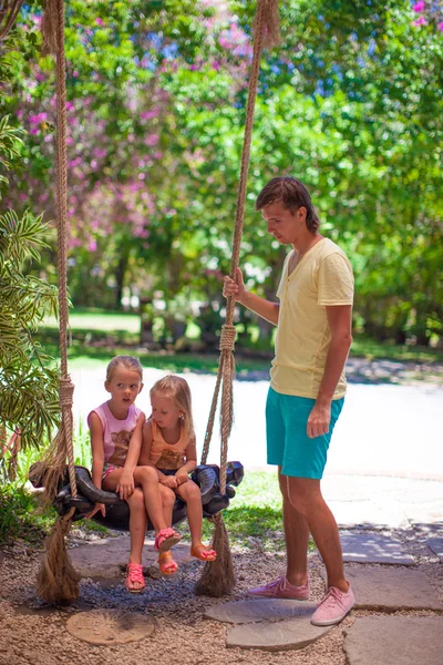 Dad shakes his young daughters on a swing in tropical hotel — Stock Photo, Image