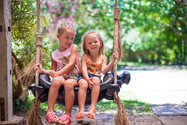 Little girls swinging in a cozy lovely flowered courtyard — Stock Photo, Image
