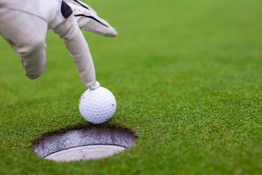 yeşil alan üzerinde delik golf topu koyarak erkek eli