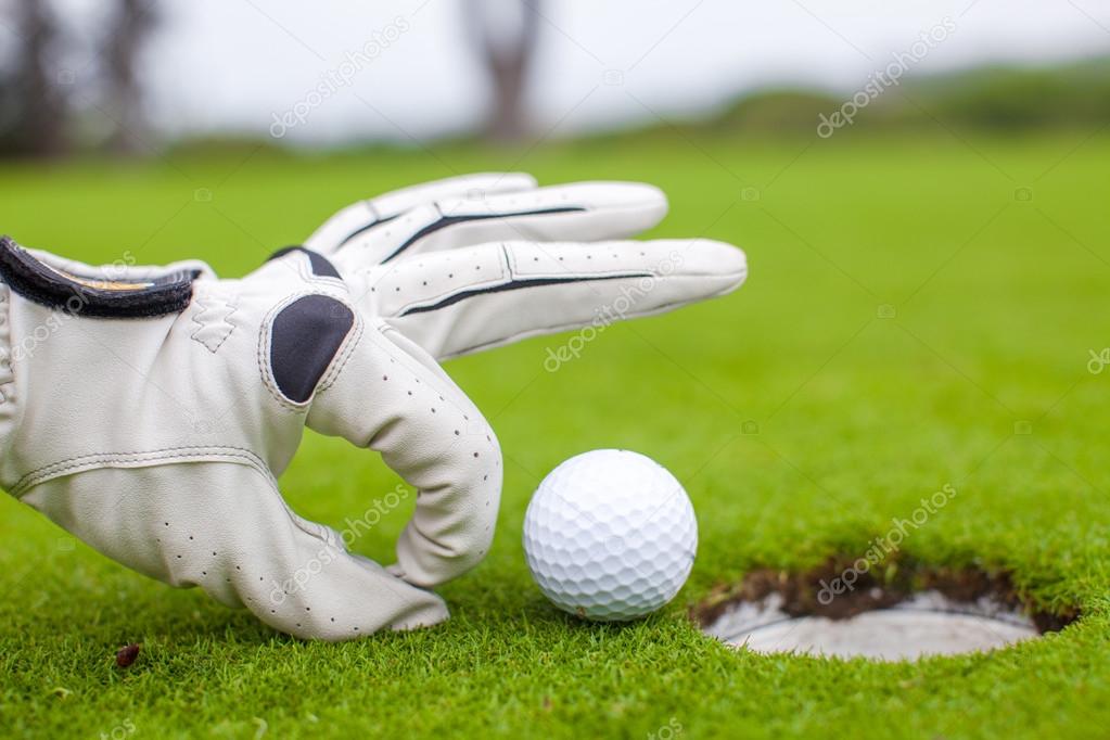Close-up of a man's hand putting golf ball in hole at course