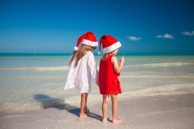 Back view of Little cute girls in Christmas hats on the exotic beach