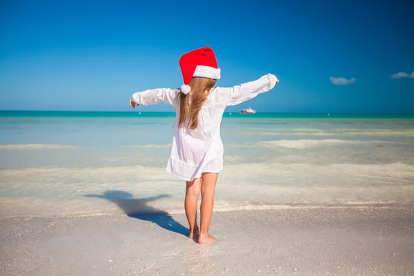 后视图的可爱的小女孩在红色帽子圣诞老人在海滩上 — 图库照片