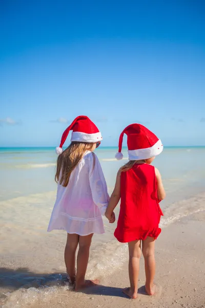 Back view of Little cute girls in Christmas hats on the exotic beach — Stockfoto