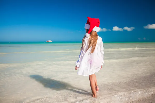 Malá roztomilá dívka v červené čepici Santa Claus na pláži — Stock fotografie