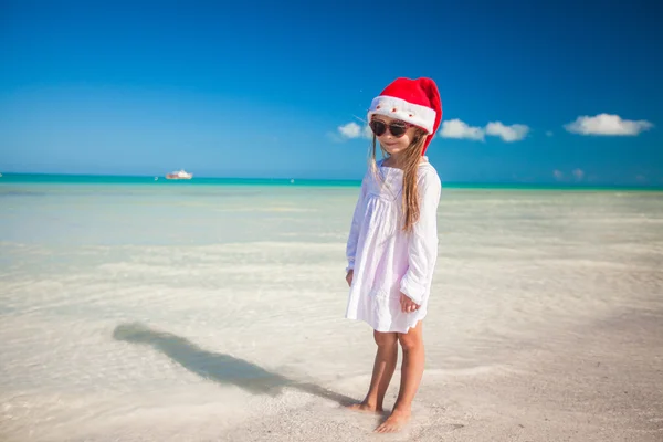 Lilla flickan i röd hatt jultomten och solglasögon på stranden — Stockfoto