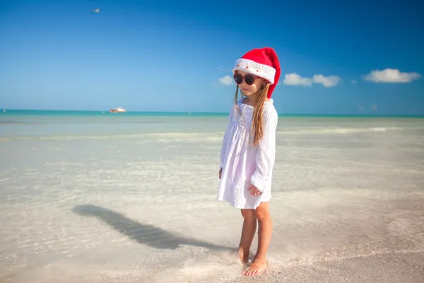 Niña en sombrero rojo Santa Claus y gafas de sol en la playa —  Fotos de Stock