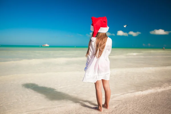 Bakifrån av lilla söta tjejen i röda hatt jultomten på stranden — Stockfoto