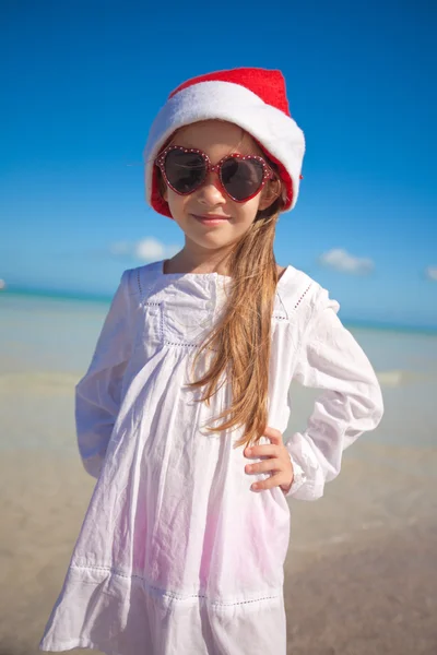 Niña en sombrero rojo Santa Claus y gafas de sol en la playa exótica —  Fotos de Stock