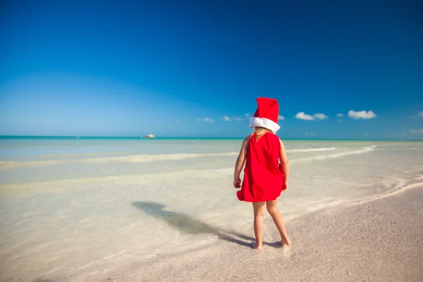 Rückansicht des kleinen süßen Mädchens mit rotem Hut Weihnachtsmann am Strand — Stockfoto