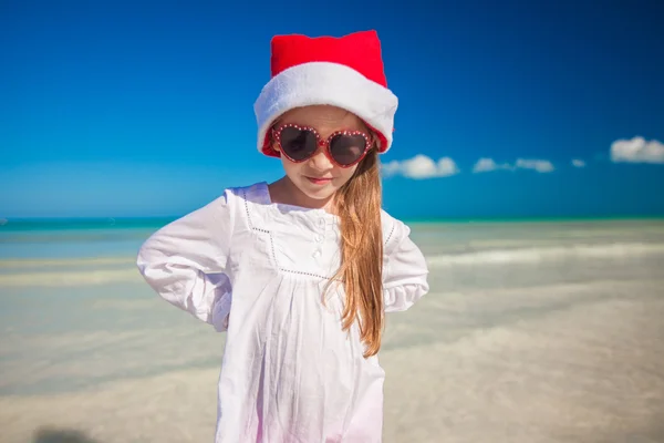 Bambina in cappello rosso Babbo Natale e occhiali da sole sulla spiaggia esotica — Foto Stock