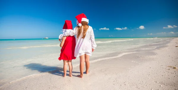 Vista trasera de las niñas lindas en sombreros de Navidad en la playa exótica —  Fotos de Stock