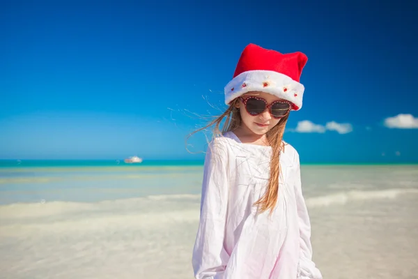 Malá holčička v červené čepice santa claus a sluneční brýle na pláži — Stock fotografie