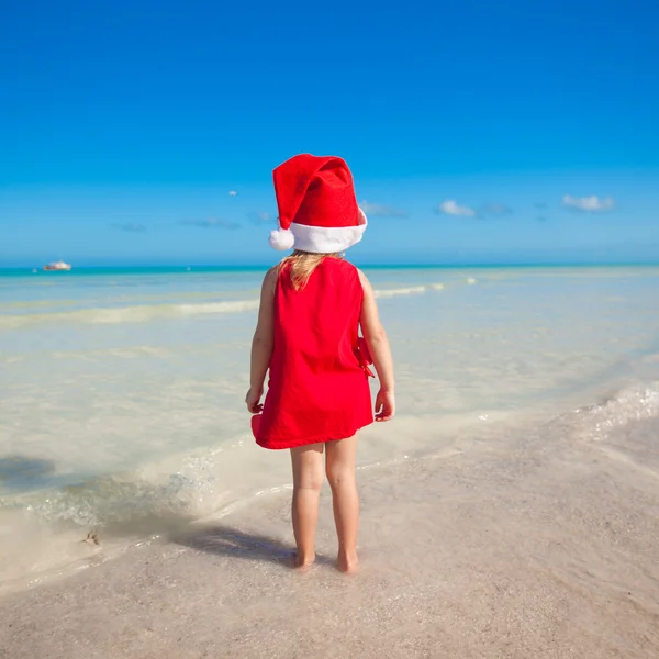 Arkadan görünüşü kırmızı küçük şirin kız plaj santa claus şapka — Stok fotoğraf