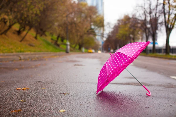 Růžový dětský deštník na mokrém asfaltu venku — Stock fotografie