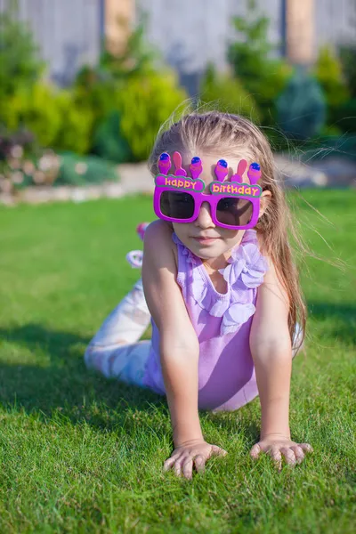 Adorable little girl with Happy Birthday glasses smiling outdoor — Stock Photo, Image