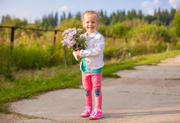 Kleines entzückendes Mädchen, das draußen mit Blumen spaziert — Stockfoto