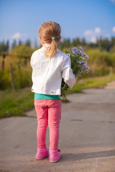 Liten söt flicka gå med en bukett blommor — Stockfoto