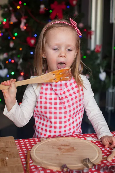 Schattig meisje eten het deeg voor gember cookies in keuken — Stockfoto