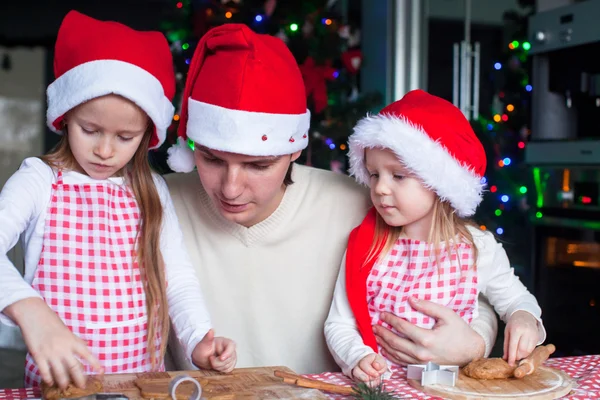 Little girls with young dad in Santa hat bake Christmas gingerbread cookies — Stock Photo, Image