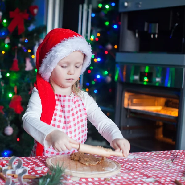 サンタ帽子でかわいい女の子クリスマスのためのジンジャーブレッドのクッキーを焼く — ストック写真