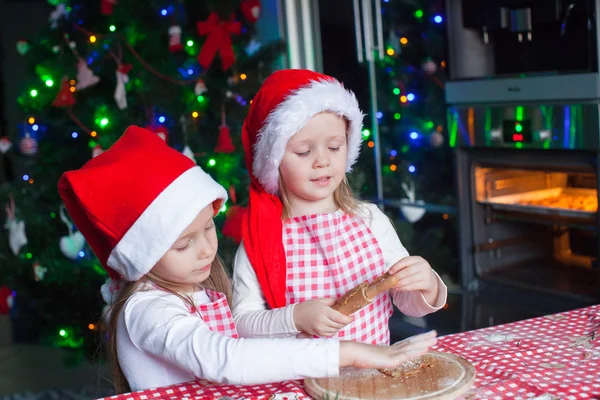 Little cute girls in Santa hats bake gingerbread cookies for Christmas — Stock Photo, Image