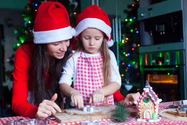 Szczęśliwa mama i mała dziewczynka w santa hat pieczenia świąteczne pierniki razem — Zdjęcie stockowe