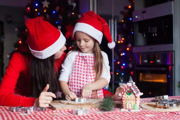 Adorable niña con madre usando sombreros de santa hornear galletas de jengibre de Navidad juntos —  Fotos de Stock