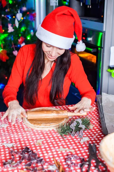 Jovem mulher no chapéu de Natal assar pão de gengibre em casa — Fotografia de Stock