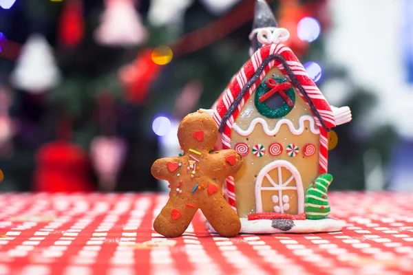 Sevimli gingerbread adamın şekerlerini önünde zencefil evin arka plan Noel ağacı ışıkları — Stok fotoğraf