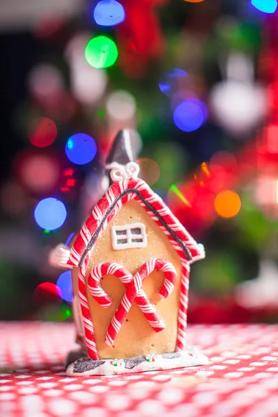 Μελόψωμο σπίτι, διακοσμημένο με πολύχρωμες καραμέλες σε φόντο του φωτεινό χριστουγεννιάτικο δέντρο με γιρλάντα — Φωτογραφία Αρχείου