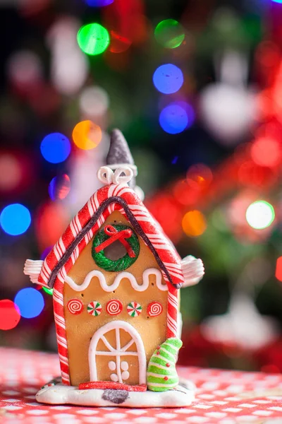 Пряничный домик феи украшен красочными конфетками на фоне яркой елки с гирляндой — стоковое фото