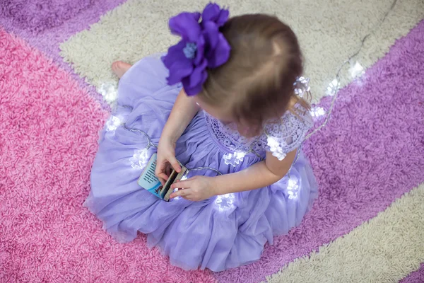 Piccola adorabile ragazza in un abito lilla tra ghirlande a casa — Foto Stock