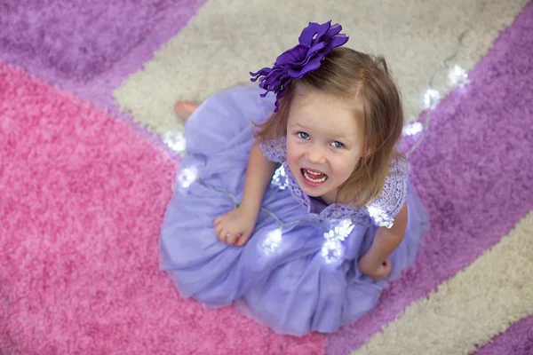 Kleines entzückendes Mädchen in schönem Kleid inmitten von Girlanden zu Hause — Stockfoto